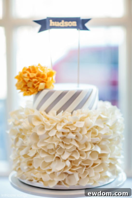 Exquisite two-tier Spirals & Poms Baby Shower Cake by Intricate Icings Cake Design, featuring a frilly pom-pom bottom tier and striped spiral top tier, on a clean background.