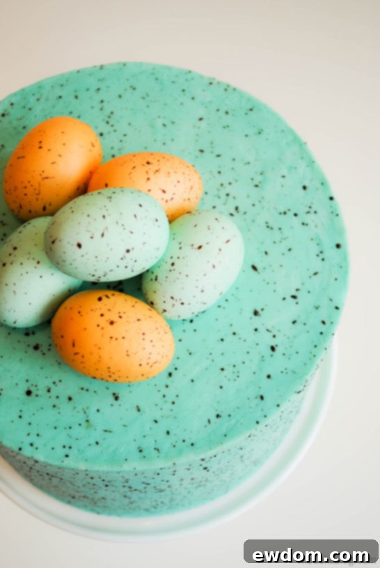 Flecked Fable Cake 6 A baker demonstrating the speckling technique on a cake, flicking chocolate paint onto the blue frosted surface. | by Carrie Sellman for TheCakeBlog.com