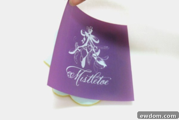 Carefully centering the mesh mistletoe stencil on a royal icing dipped cookie