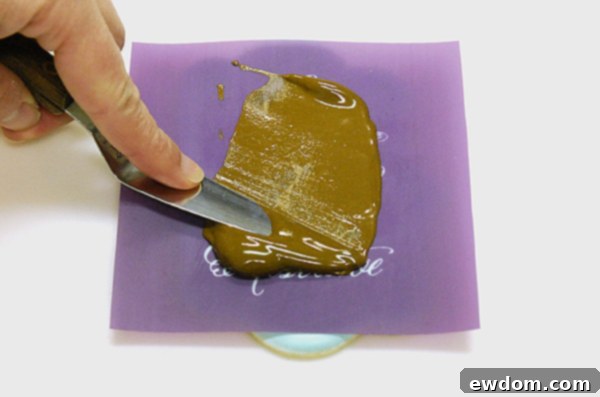 Spreading thinned royal icing over the stencil and scraping off excess