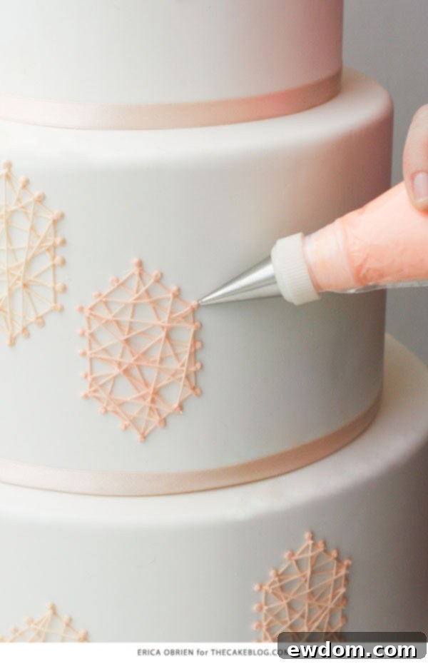 Detailed shot of royal icing string art being carefully piped onto the cake, illustrating the precise geometric patterns.