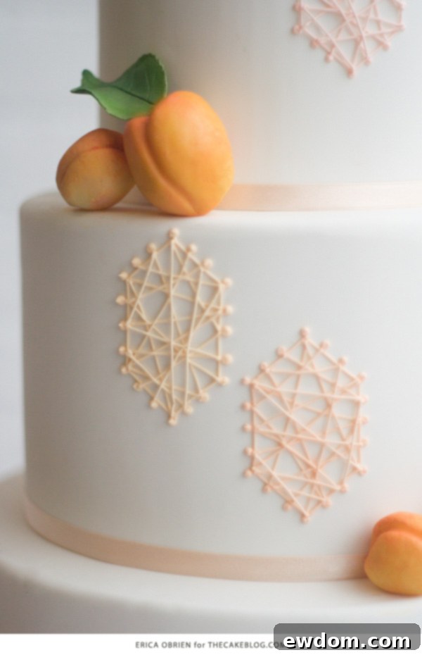 An artisan's hand expertly applies delicate royal icing strings, building the intricate geometric design of the peach cake.