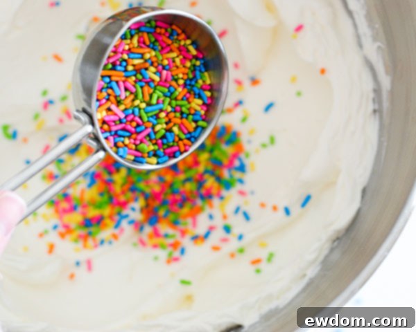 Adding assorted jimmie sprinkles to Swiss Meringue Buttercream frosting for the DIY sprinkle cake, a key component for vibrant Graduation Party Desserts.