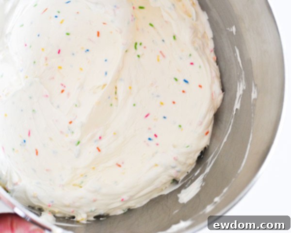 Folding jimmie sprinkles into buttercream, preparing the colorful frosting for a festive DIY sprinkle cake among Graduation Party Desserts.