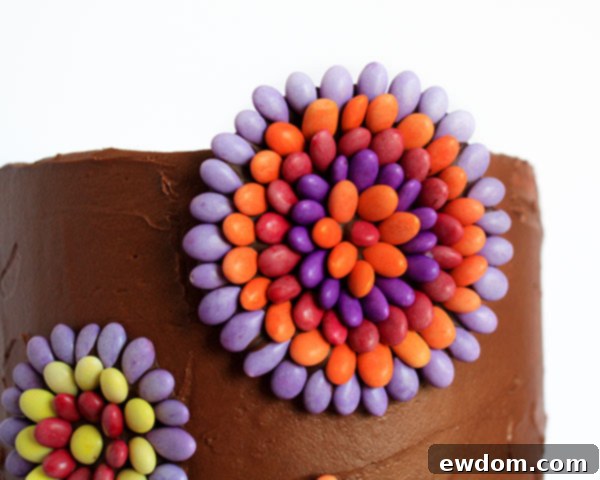 Artist's hand gently pressing a finished chocolate sunflower seed medallion onto the buttercream side of a cake, showing final decorative step