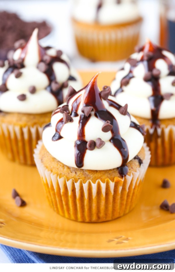Stack of pumpkin chocolate chip cupcakes with creamy frosting and chocolate sauce drizzle