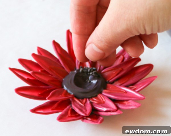 Dusting the chocolate sunflower center with crushed black sprinkles for texture