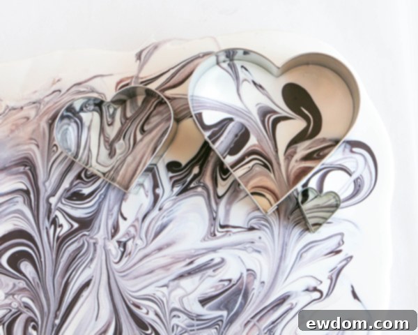 Heart-shaped cookie cutters pressed into the setting marbled chocolate, showing the initial stage of cutting out the toppers.