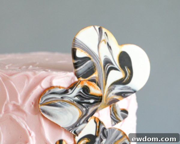 A close-up of a marbled chocolate heart securely attached to a pale pink buttercream cake, showcasing its final elegant presentation as a cake topper.