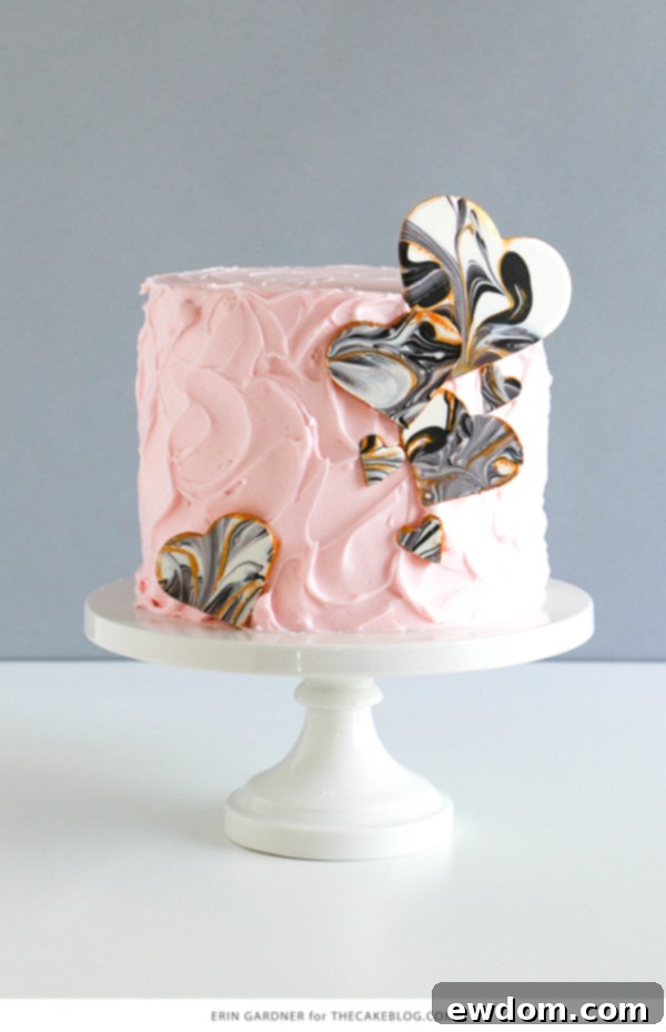 A stunning pale pink cake elegantly decorated with various sizes of black and white marbled chocolate hearts, highlighting their versatile application as edible cake decorations.