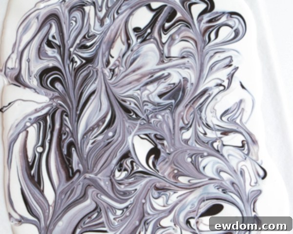 Using a small knife to gently swirl the black and white chocolates together, showcasing the creation of the intricate marbled design.