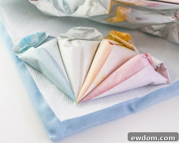 Elegant Swirl Easter Chocolates 7 Piping bags filled with colorful melted chocolate resting on a foil-covered heating pad to maintain warmth and fluidity.