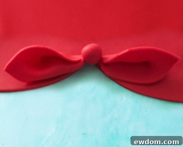 Matryoshka Magic Cake 14 Detailed view of the finished red fondant bow on the Russian nesting doll cake, adding a charming accent. Cake by Cakegirls.