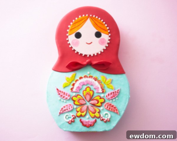 Matryoshka Magic Cake 20 Final assembly of the Russian nesting doll cake: attaching the face, arranging appliques, and piping decorative buttercream dots. Cake by Cakegirls.