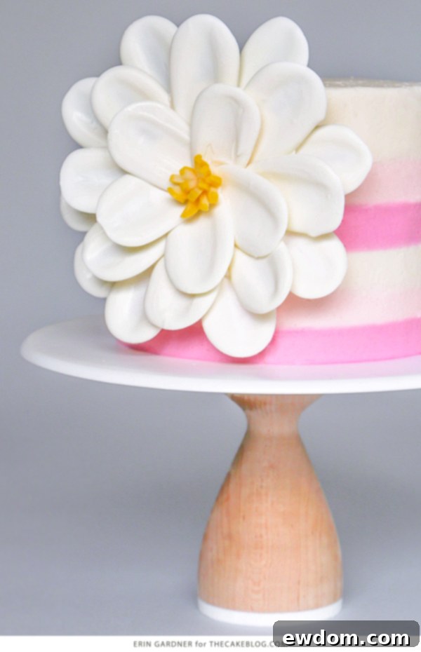 A close-up view of the finished white chocolate flower artfully placed on the side of a cake, showing its elegant and detailed structure.