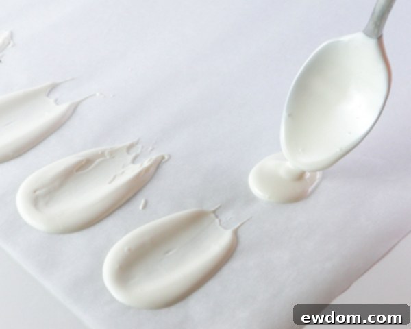 First step of petal creation: melted white chocolate is spooned onto parchment paper to begin forming the flower petals.