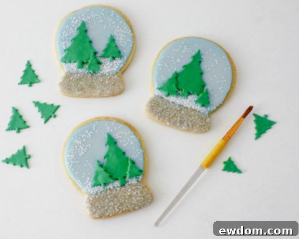 Decorating Snow Globe Cookies - Attaching fondant Christmas trees to the dried glazed cookies by Cakegirls for TheCakeBlog.com