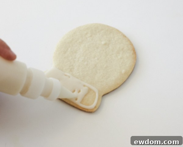 Decorating Snow Globe Cookies - Piping white cookie glaze for the base of the snow globe design by Cakegirls for TheCakeBlog.com