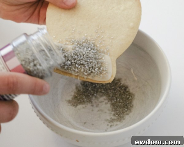 Decorating Snow Globe Cookies - Adding silver sugar crystals to the wet white glaze base for a sparkling effect by Cakegirls for TheCakeBlog.com