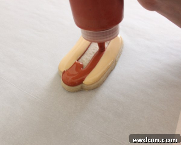 Adding red royal icing ketchup squiggle to hot dog cookie