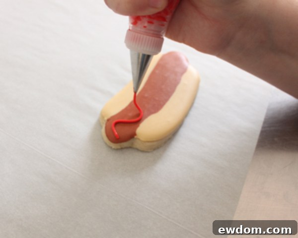 Adding yellow royal icing mustard squiggle to hot dog cookie