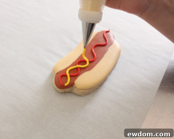 Sprinkling lime green jimmies for relish on hot dog cookies