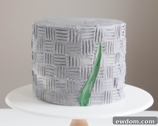 Refining the green buttercream stems on the cake, showing smooth application