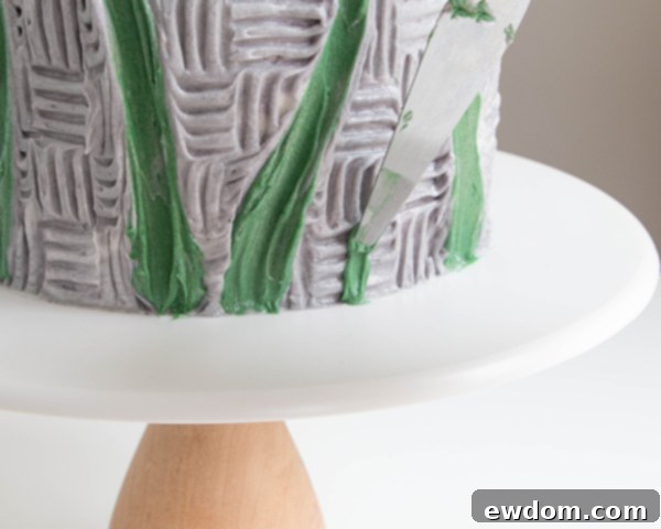 Adding small blades of grass to the cake base with green buttercream and a tapered spatula