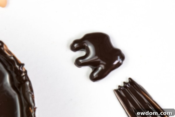 A chocolate-dipped animal cracker being carefully placed onto parchment paper to dry and set, preventing puddles around the cookie | by Erin Gardner for TheCakeBlog.com
