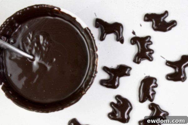 A collection of freshly chocolate-dipped animal crackers drying on parchment paper, awaiting their white chocolate skeletal details | by Erin Gardner for TheCakeBlog.com