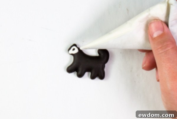 Piping white chocolate skeletal details onto a dark chocolate-dipped animal cracker, transforming it into a charmingly spooky skeleton for the cake | by Erin Gardner for TheCakeBlog.com