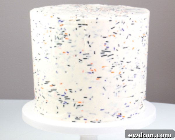 Applying sprinkle-infused buttercream to the sides of a crumb-coated cake, creating a textured and colorful foundation for the Halloween design | by Erin Gardner for TheCakeBlog.com