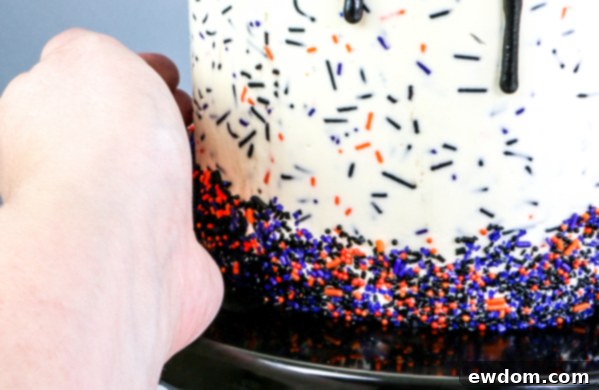 Applying a vibrant Halloween sprinkle mix to the bottom edge of the frosted cake, creating a festive and colorful border | by Erin Gardner for TheCakeBlog.com