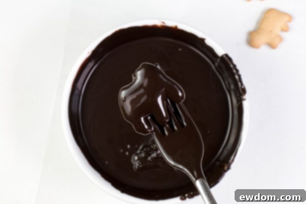 Excess chocolate being tapped off an animal cracker on a fork, a technique to achieve a clean and even coating for the spooky skeletons | by Erin Gardner for TheCakeBlog.com