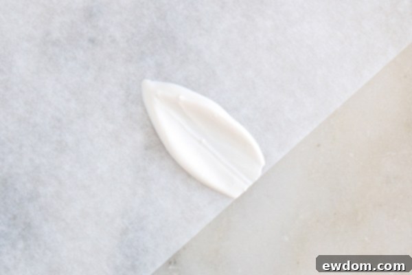 Multiple white chocolate bunny ears neatly lined up on parchment paper, allowing them to set.