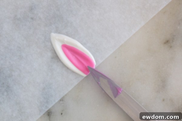 Applying pink chocolate to the center of a white chocolate ear, leaving a white border.