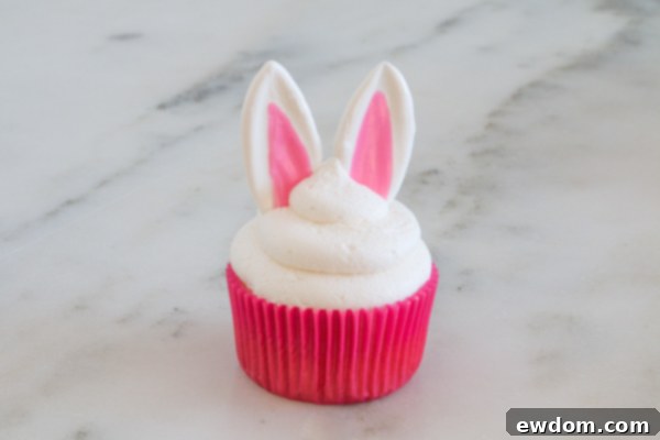 Gently pressing hardened chocolate bunny ears into the fresh buttercream frosting of a cupcake.