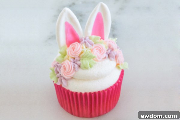 A finished Easter Bunny Cupcake showing the chocolate ears, buttercream floral headband, and vibrant colors.