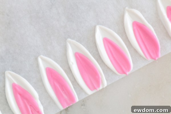Process shot showing a knife coated with melted white chocolate, ready to create bunny ears on parchment paper.