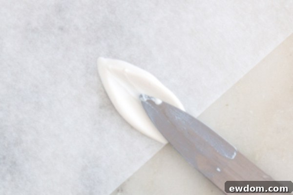 A close-up of a perfectly formed white chocolate bunny ear cooling on parchment paper.